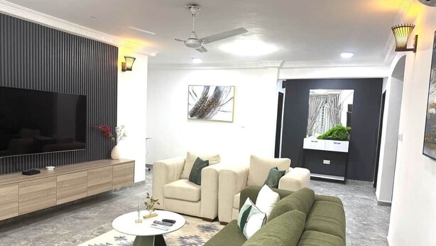 Ein modernes Wohnzimmer mit Flachbildfernseher, einer Sofagarnitur, einem Couchtisch und einem Deckenventilator.