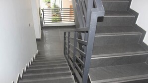 Una escala de metall amb barana i trams negres que condueix a una zona exterior amb barana i plantes en testos.