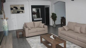Uma sala de estar com dois sofás, uma mesa de centro, uma mesinha e um vaso de planta.