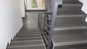 Uma escada com degraus pretos e corrimão de metal.