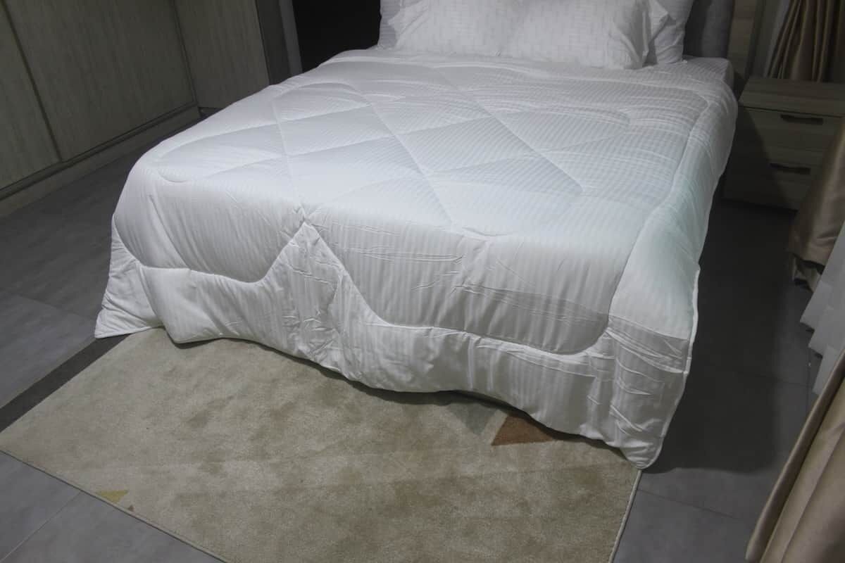 Een net opgemaakt bed met een witte sprei en een beige vloerkleed.