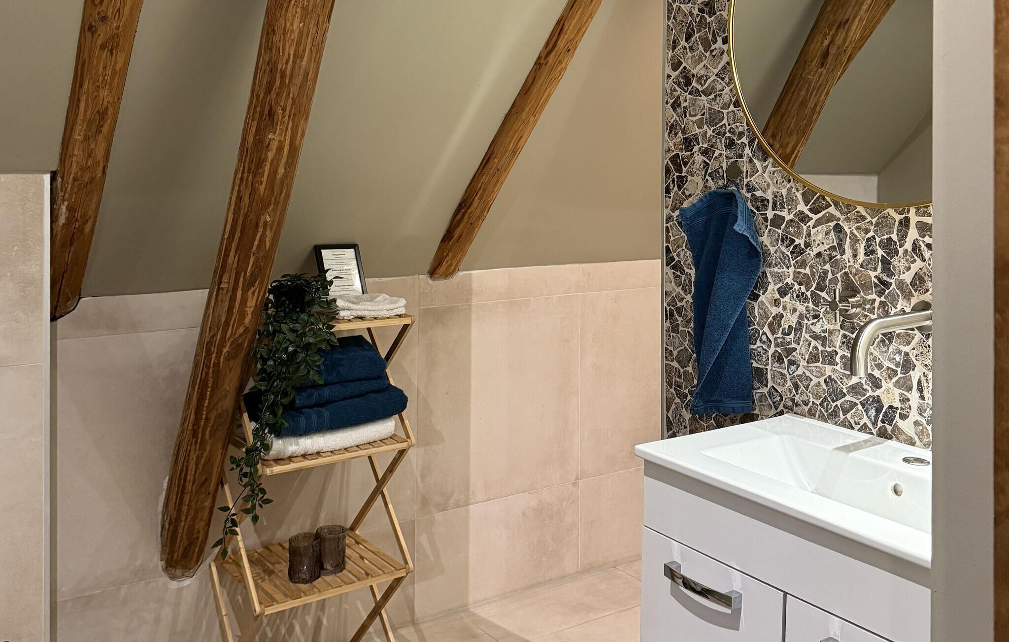 A bathroom with a white sink, a mirror with a mosaic backsplash, and wooden beams on the ceiling.