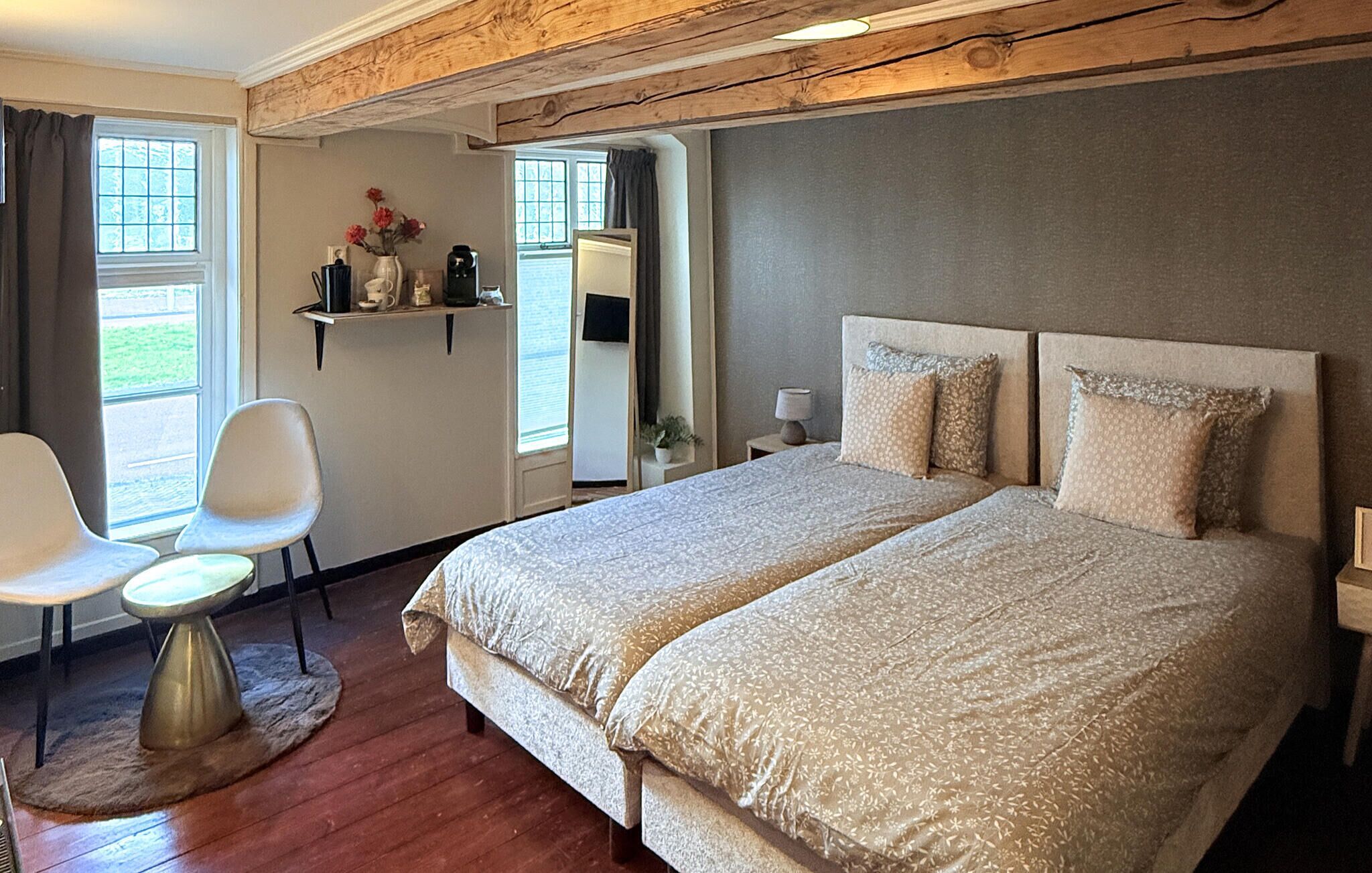 A hotel room with a large bed, two bedside tables, a chair, a small table, and a shelf with flowers.