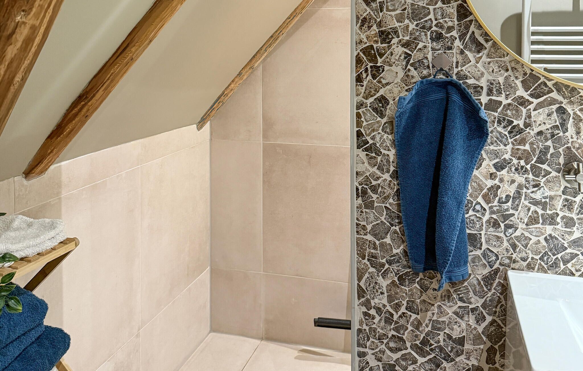 A bathroom with beige tiles, a wooden ceiling beam, a shower area, and a mosaic tile wall.