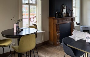 Een eethoek met een ronde tafel, gele stoelen, een zwarte tafel en een open haard met decoratieve objecten.
