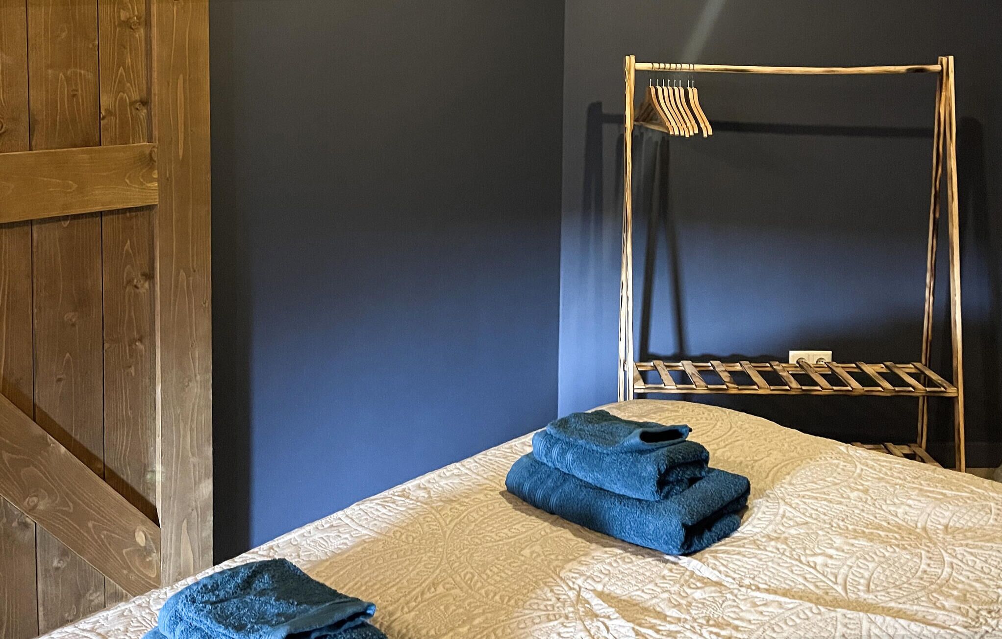 Une pièce comprenant un lit, une armoire en bois et un portant métallique avec des vêtements.