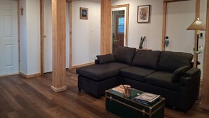 Un salon comprenant un canapé d’angle, des poutres en bois, une lampe et une petite table sur laquelle sont posés des livres et un objet décoratif.