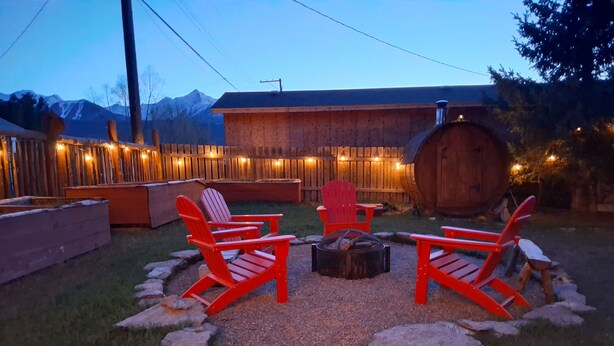 Une terrasse en bois avec des fauteuils Adirondack, un foyer et un bâtiment rustique agrémenté d’un tonneau.