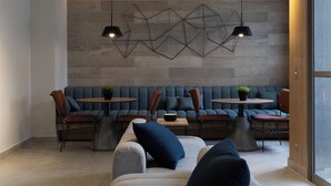 Ein modernes Interieur mit einer Sitzecke, ausgestattet mit Sofas und Sesseln, einem Couchtisch und einem geometrischen Wandbild.
