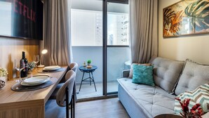 Ein modernes Wohnzimmer mit einer Couch, einem Esstisch mit Tellern und Gläsern, einem kleinen Beistelltisch und einem an der Wand montierten Fernseher.
