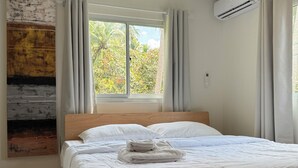 Une chambre dotée d’un grand lit, d’une fenêtre avec des rideaux, d’un climatiseur et d’une œuvre d’art accrochée au mur.
