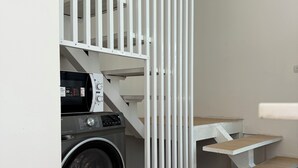 Un espace buanderie comprenant un lave-linge, un étendoir et un escalier blanc.