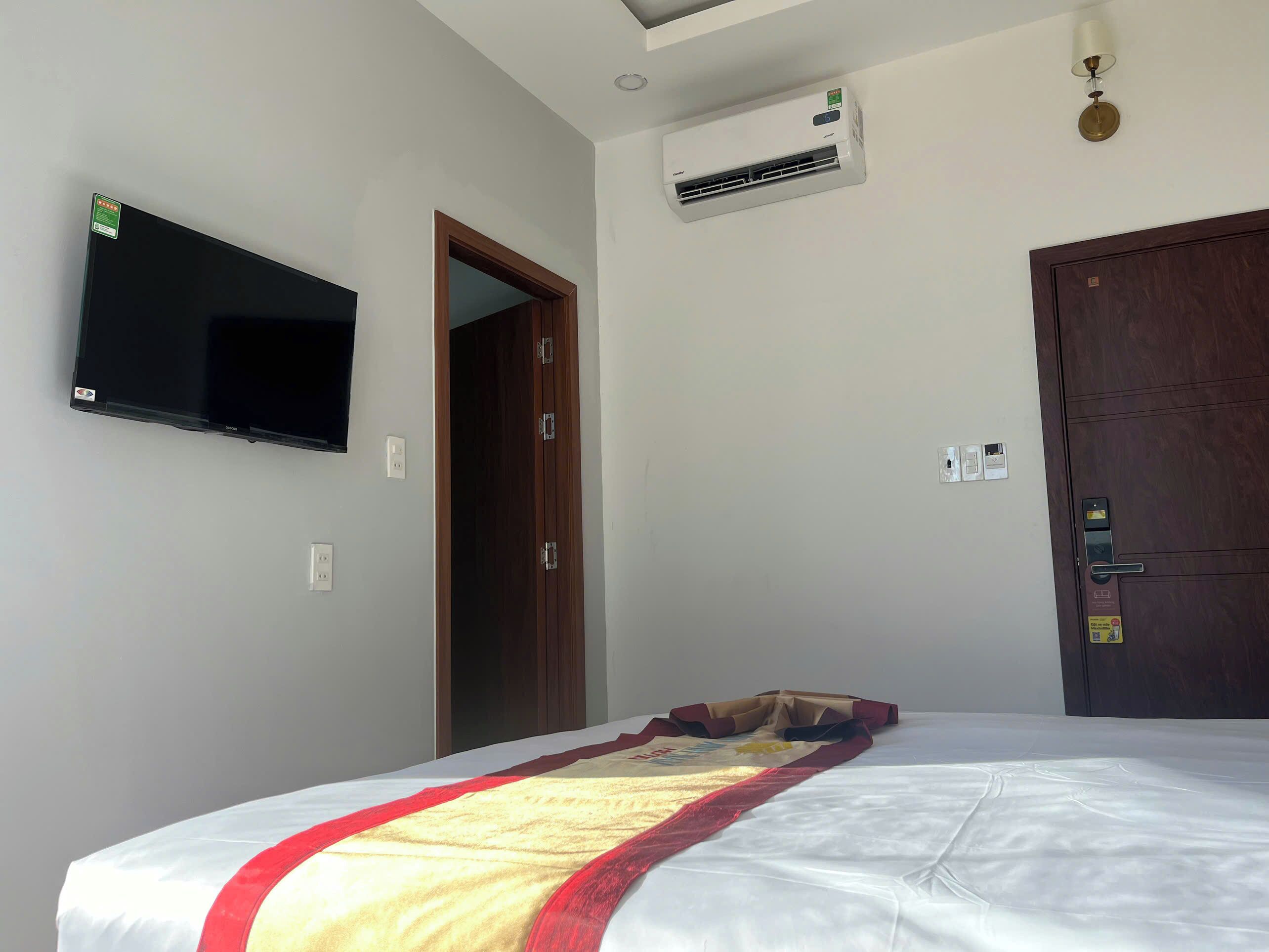 Un dormitorio con cama, televisor montado, aire acondicionado, una puerta y una lámpara.