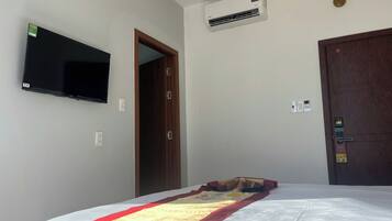 Un dormitorio con cama, televisor montado, aire acondicionado, una puerta y una lámpara.