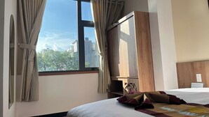 A hotel room with a large window, a bed with a white bedspread and decorative pillows, a wooden headboard, and a wall-mounted TV. - MINH MINH NAM 3 HOTEL (Can Tho)