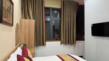 Una camera d'albergo con un letto, tende, una televisione e una finestra.