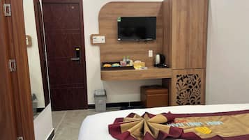 A hotel room with a wooden desk, a television, a small trash bin, and a bed with a decorative headboard.