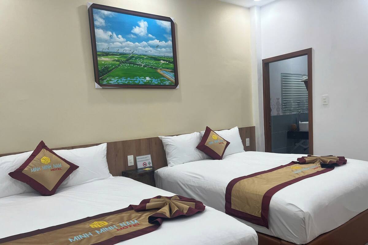 A hotel room with two beds, each with a white bedspread and a brown and maroon bed runner with the hotel logo. A painting of a landscape is on the wall above the beds.