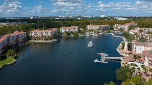 A large body of water surrounded by multi-story buildings with balconies, a dock, and a fountain.