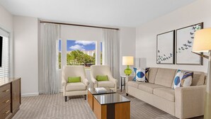 A hotel room with two armchairs, a sofa, a coffee table, a lamp, and artwork on the wall.