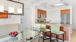 A modern kitchen with a glass dining table, wooden chairs, a built-in oven, and a stainless steel refrigerator.