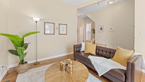 A living room with a brown leather sofa, a round coffee table, and a large green plant. - Charming KC 2BR 1 BATH Downtown Access In-Unit Laundry (Kansas City)
