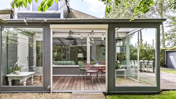Eine moderne, ganzheitig verglaste Terrasse mit Holzdeck, Gartenmöbeln und Blick auf den Hinterhof.