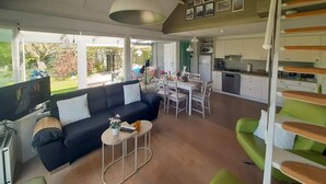 Ein modernes Wohnzimmer mit einer Couch, Couchtisch und Sesseln, ein Essbereich mit Tisch und Stühlen sowie eine Küche mit Schränken und Geräten.