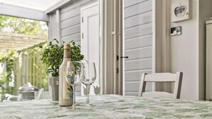 Ein Tisch mit einer Flasche und zwei Gläsern, ein Stuhl und eine Tür in einem überdachten Außenbereich.