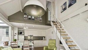 Eine moderne Küche mit weißen Schränken, ein Essbereich mit Tisch und Stühlen sowie eine Treppe mit Holzdielen.