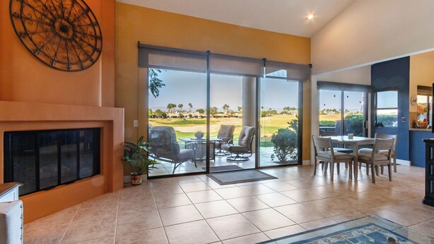 A spacious living area with a large window offering a view of a golf course, a fireplace, and a dining area with chairs and a table. - Hacienda-Resort Style-Golf, Music, & Art Paradise in La Quinta, PGA West Stadium (La Quinta)