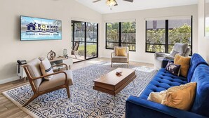 Ein geräumiges Wohnzimmer mit einem blauen Sofa, einem Holztisch und einem gemusterten Teppich.
