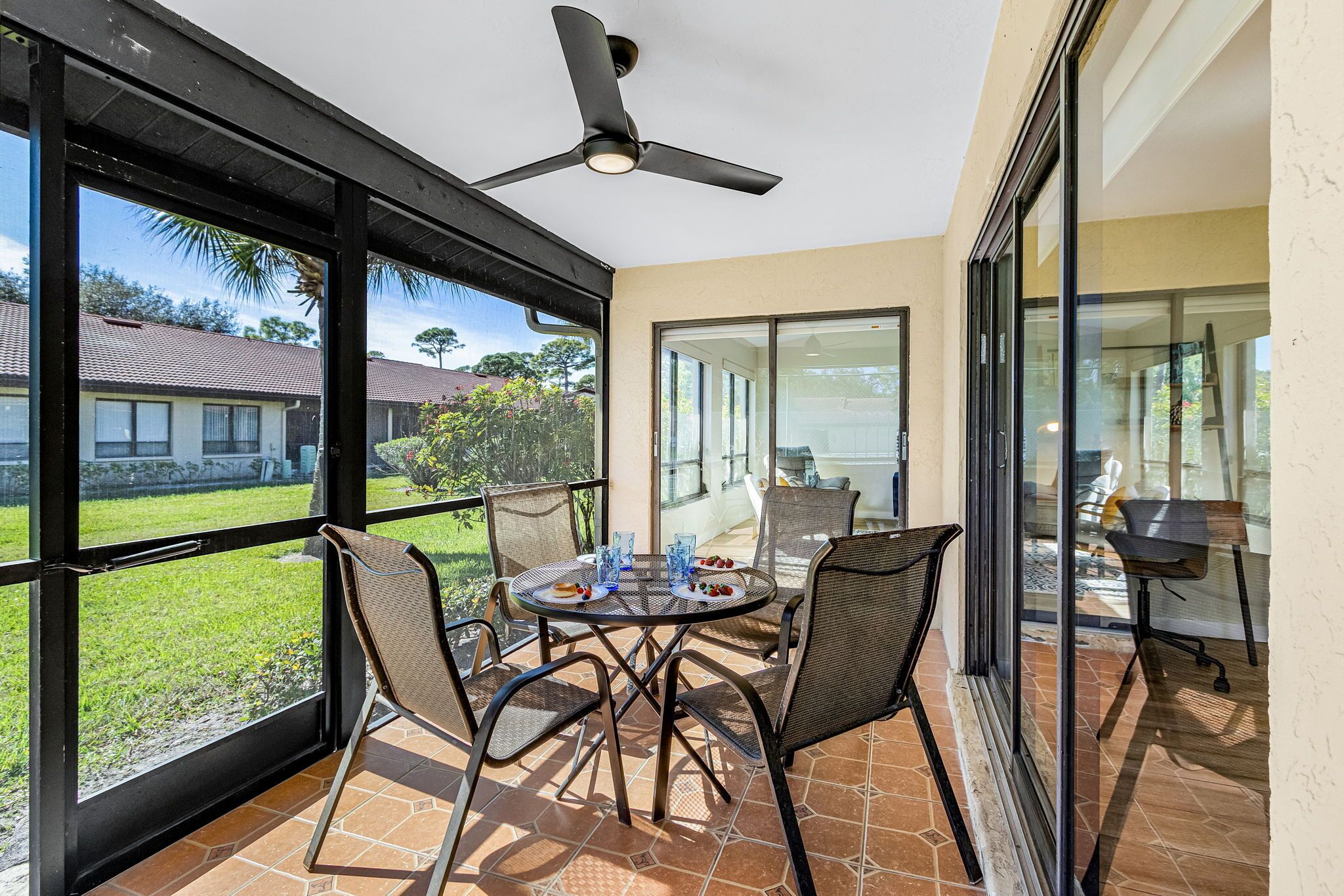 A balcony with a table and chairs, a ceiling fan, and large windows offering a view of the surrounding area.