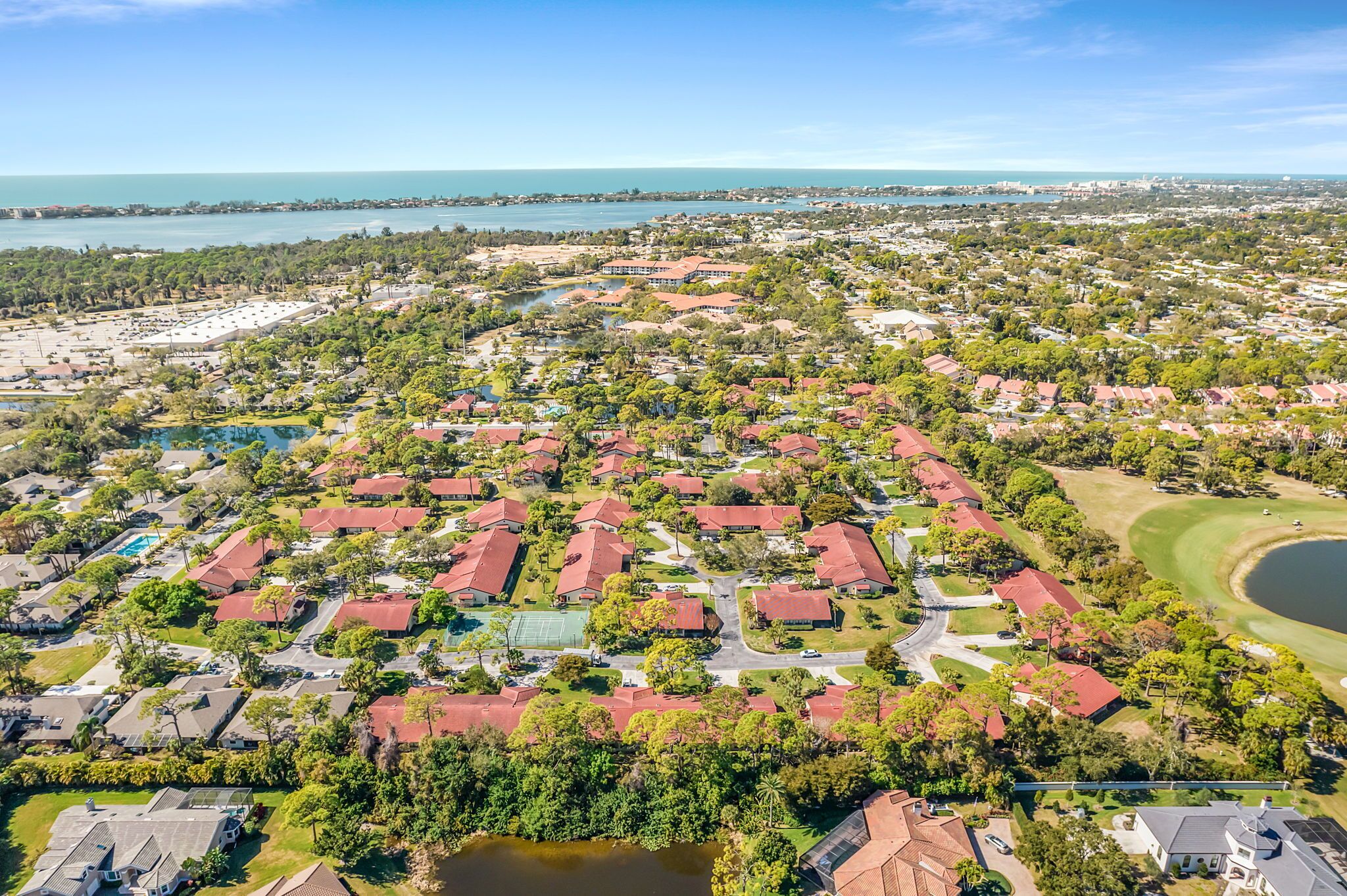 An aerial view of a residential area with houses, a golf course, and a large body of water.