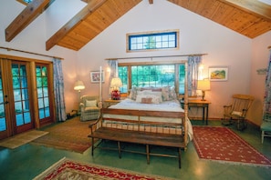 A bedroom with a wooden bed, two bedside tables, a rocking chair, a window with curtains, and a view of greenery outside. - A Private Sierra Lake Sanctuary — Truly An Unforgettable Vacation Experience (North Fork)