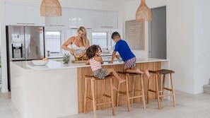 A modern kitchen with a central island, wooden stools, and a stainless steel refrigerator. - Daybreak Shores (Casuarina)