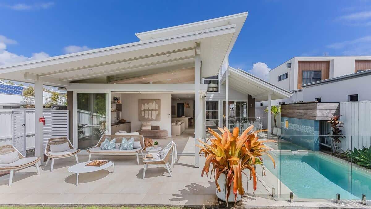 Une maison moderne dotée d’un patio couvert, d’une piscine et de mobilier d’extérieur.