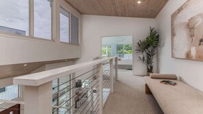 A modern interior with a glass railing, a bench, and a large window. - Daybreak Shores (Casuarina)
