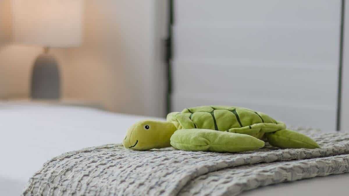 Une peluche en forme de tortue est posée sur un lit recouvert d’une couverture à motifs.