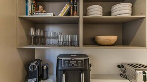 A kitchen area with a coffee maker, toaster, and a shelf with books and dishes. - Daybreak Shores (Casuarina)