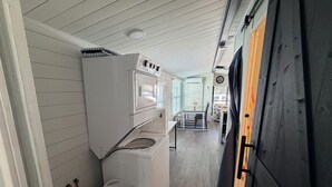 Ett tvättrum med tvättmaskin och torktumlare, en tvättkorg och en dörr som leder till matplatsen.