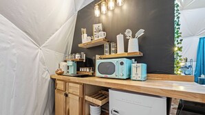 Ett kompakt kök med mikrovågsugn, brödrost och ett litet kylskåp. Köket har träskåp och en bänkskiva med diverse köksredskap.