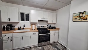 A compact kitchen with white cabinets, a stove, oven, and a sink. - Central and Convenient Ground Floor Apartment (Oswego)