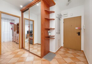 Hotellihuone, jossa on puinen ovi, peili, puinen hyllykkö, puhelin ja laattalattia.