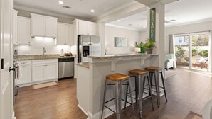 Una cocina moderna con armarios blancos, un refrigerador de acero inoxidable y una zona de bar con taburetes.