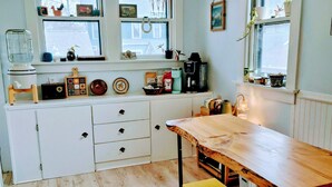 Een keuken met een houten tafel, een gele kruk, witte kastjes en een hangende lamp.