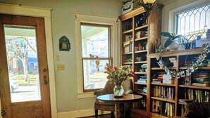 Een gezellige woonkamer met houten vloeren, een kamerkleed met patroon, een houten salontafel, een boekenkast en een deur naar buiten.