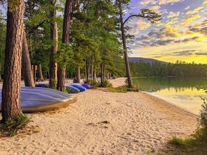 Une plage où l’on aperçoit des kayaks alignés et des arbres en arrière-plan.