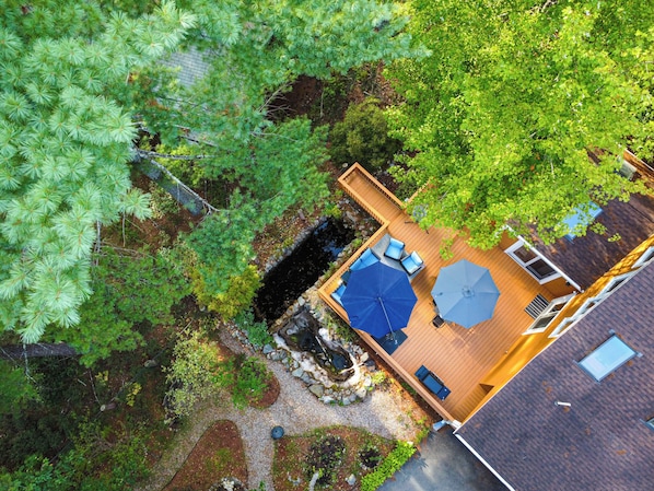 Vue aérienne d’une terrasse en bois avec des sièges d’extérieur et un petit étang.