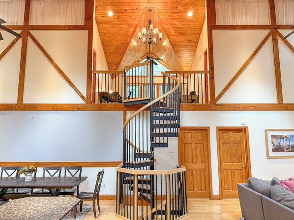 A spacious interior with a central spiral staircase, wooden beams, and a chandelier.